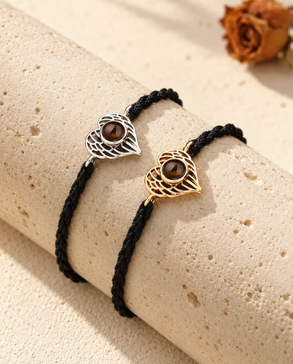 Pulseras de corazón de alas de ángel en plateado y dorado, una junto a otra sobre un bloque de travertino