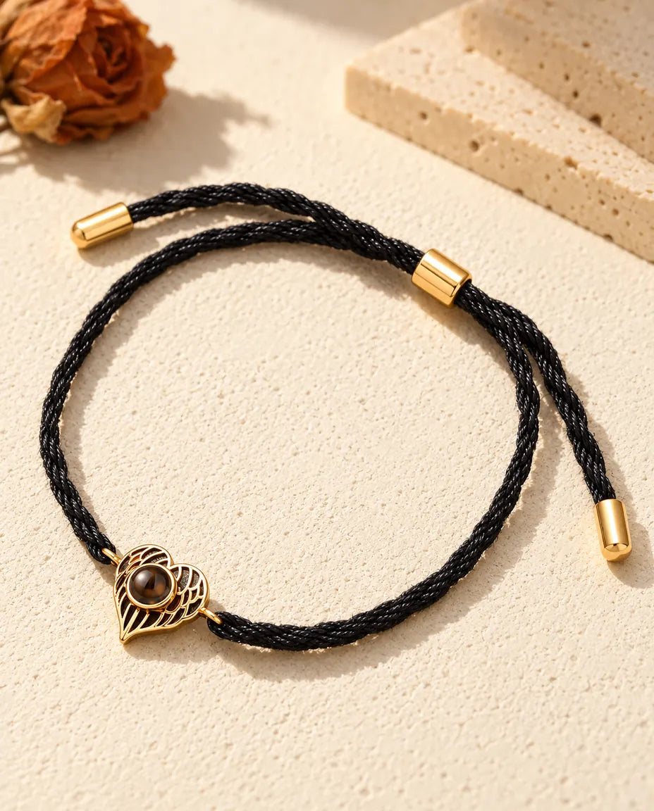 Pulsera recuerdo de corazón de alas de ángel dorado en cordón negro torcido, con pasador y puntas de metal