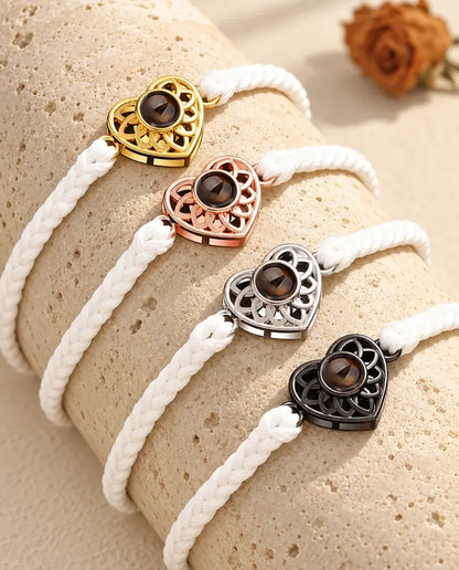 Cuatro pulseras de cordón fino blanco con corazón dorado, color oro rosa, plateado y negro sobre travertino
