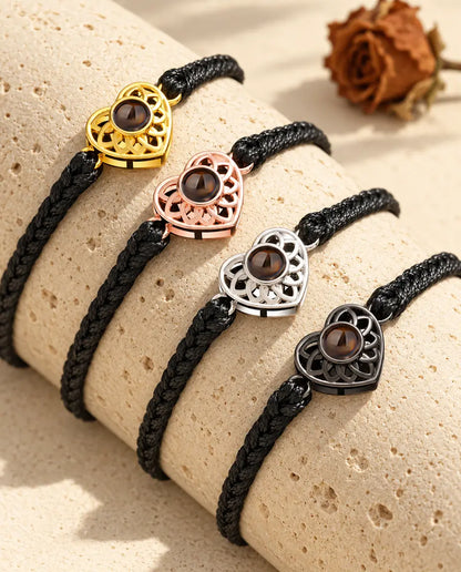 Cuatro pulseras de cordón trenzado fino negro con todos los colores de corazón, colocadas sobre travertino