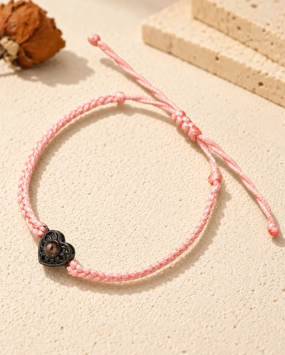 Pulsera de cordón trenzado fino rosa con corazón negro que sujeta una pequeña piedra marrón de proyección
