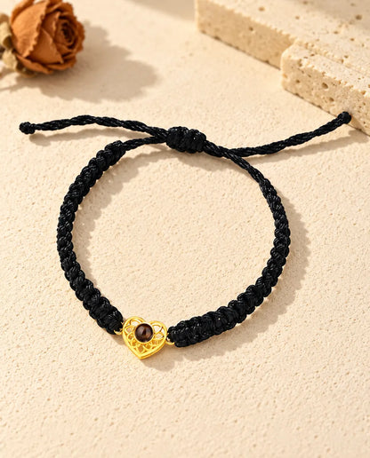 Vista cenital de la pulsera de corazón dorado en cordón trenzado negro, con el nudo corredizo y sus extremos