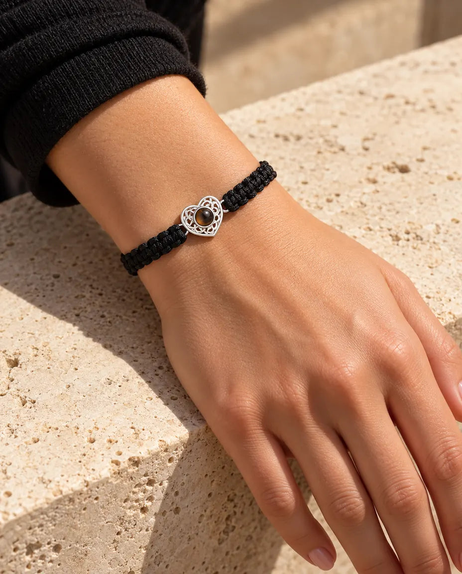 Mujer con la pulsera de cordón trenzado negro y corazón plateado en la muñeca, bajo una cálida luz de sol