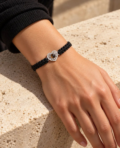 Mujer con la pulsera de cordón trenzado negro y corazón plateado en la muñeca, bajo una cálida luz de sol