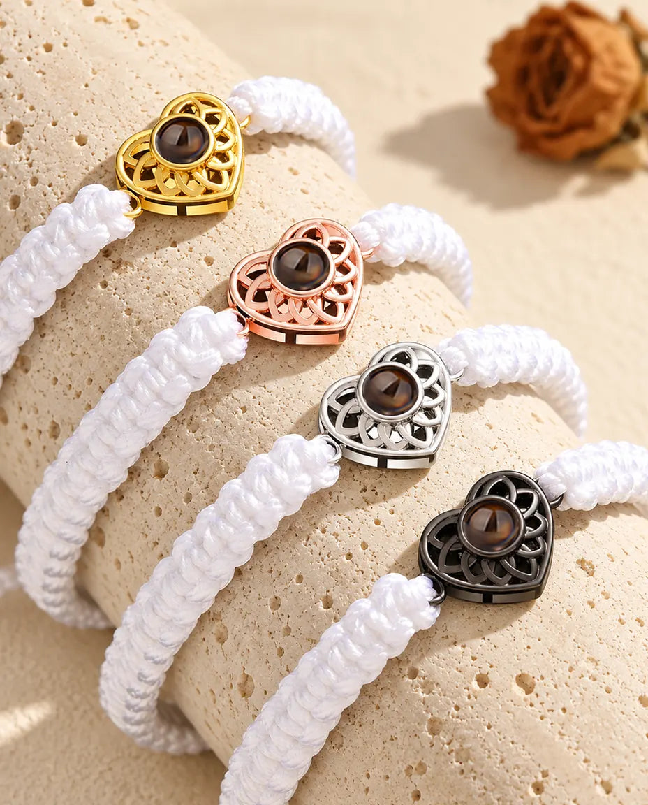 Cuatro pulseras de cordón trenzado blanco con corazón dorado, color oro rosa, plateado y negro sobre travertino