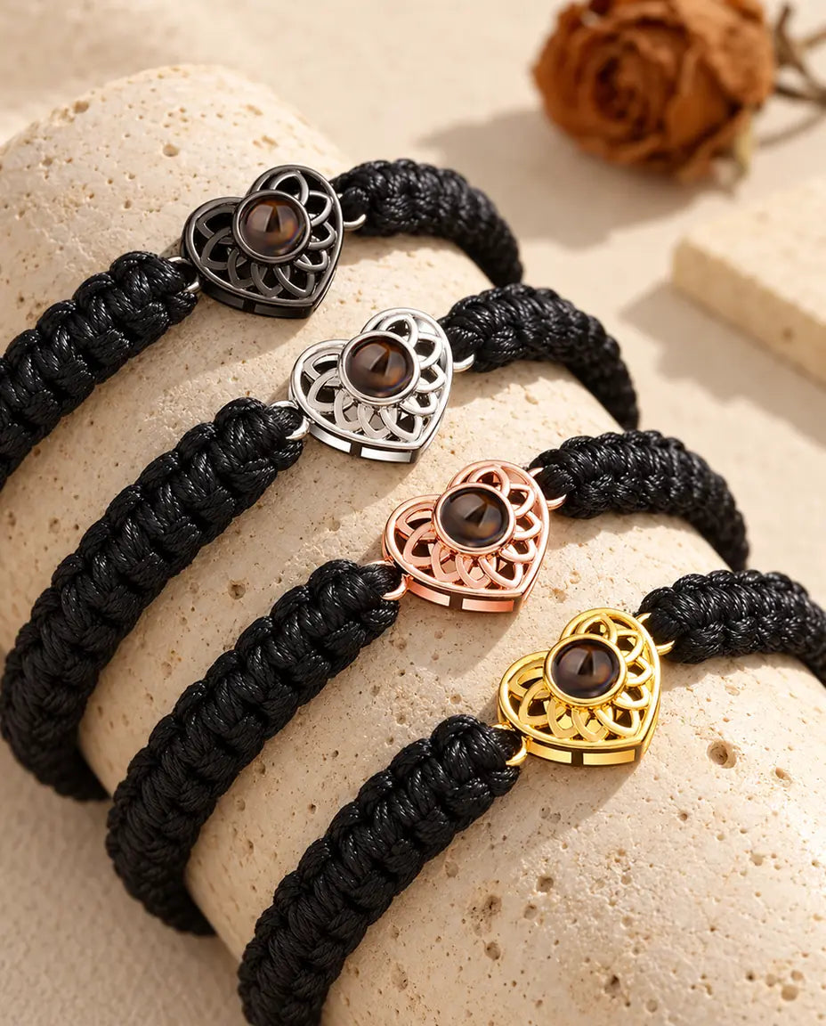 Cuatro pulseras de cordón trenzado negro con todos los colores de corazón, colocadas sobre travertino