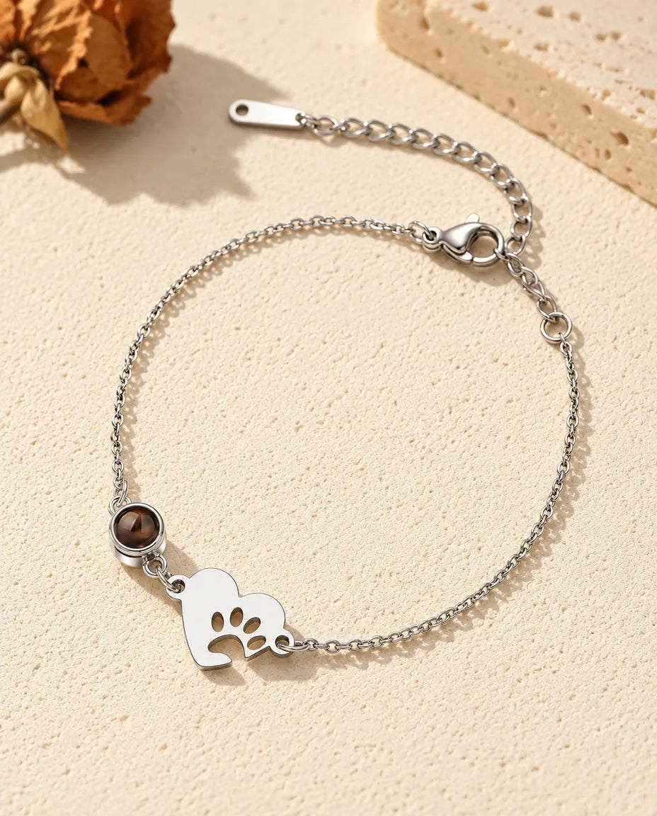 Pulsera con foto dentro personalizada: corazón plateado con huella de pata y piedra en cadena fina, sobre yeso crema