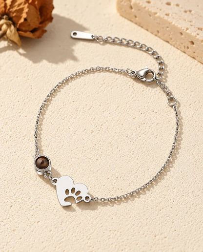 Pulsera con foto dentro personalizada: corazón plateado con huella de pata y piedra en cadena fina, sobre yeso crema
