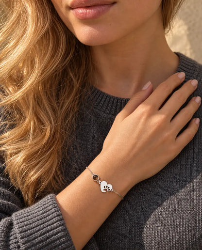 Mujer con las yemas de los dedos en la clavícula, con la pulsera de corazón plateado con huella de pata