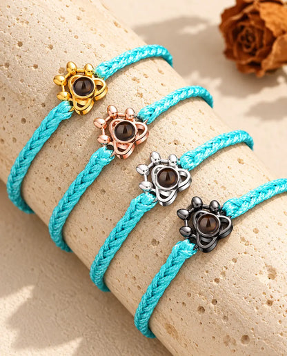 Cuatro pulseras de cordón trenzado azul con huella dorada, color oro rosa, de plata y negra sobre travertino
