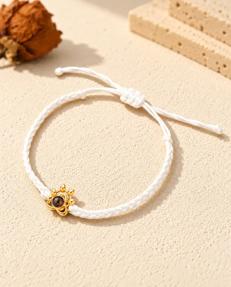 Pulsera con foto dentro de cordón trenzado blanco, con colgante huella dorado y nudo corredizo
