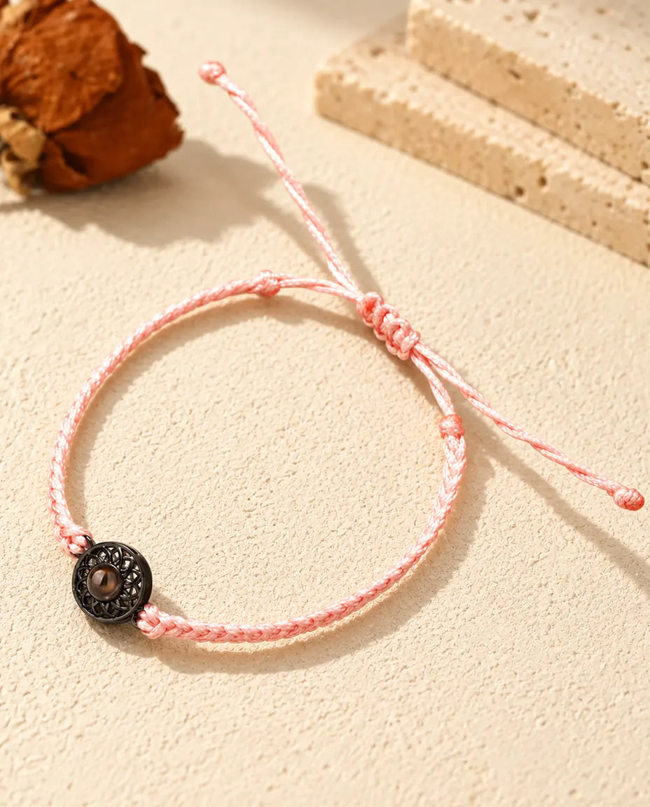 Pulsera de cordón trenzado fino rosa con círculo negro que sujeta una pequeña piedra marrón de proyección