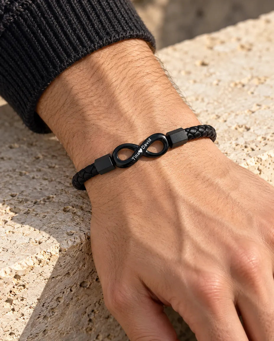 Hombre con la pulsera de cuero sintético trenzado e infinito negro grabado en la muñeca, junto a un jersey de punto gris antracita