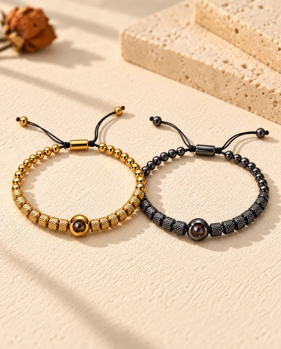 Pulseras de pareja con foto dentro: juego de dos pulseras de cuentas texturadas, dorada y negra, sobre yeso crema