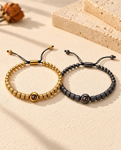 Pulseras de pareja con foto dentro: juego de dos pulseras de cuentas texturadas, dorada y negra, sobre yeso crema