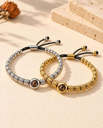 Pulseras de cuentas plateada y dorada entrelazadas como dos anillos sobre yeso crema