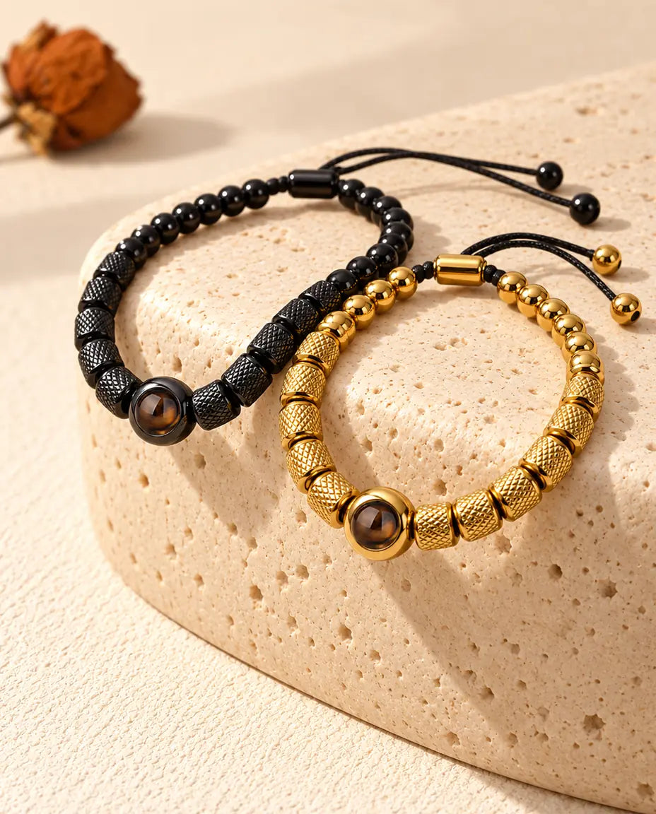 Pulseras de pareja de cuentas en negro y dorado colgando sobre un bloque de travertino